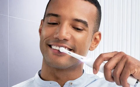 Man die zijn tanden poetst met een witte Oral-B elektrische tandenborstel, glimlachend en met een gezonde mondhygiëne.