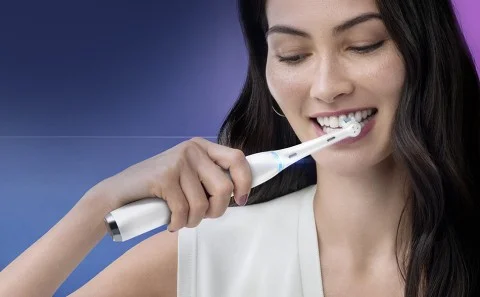 Oral-B elektrische tandenborstel in gebruik, een vrouw poetst haar tanden en lacht.