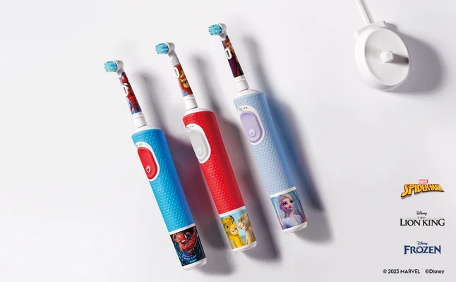 Three colorful electric toothbrushes are displayed side by side, featuring designs of Spider-Man, The Lion King, and Frozen characters, with a white charging base visible in the background; logos for Marvel, Disney, The Lion King, and Frozen are positioned at the bottom.